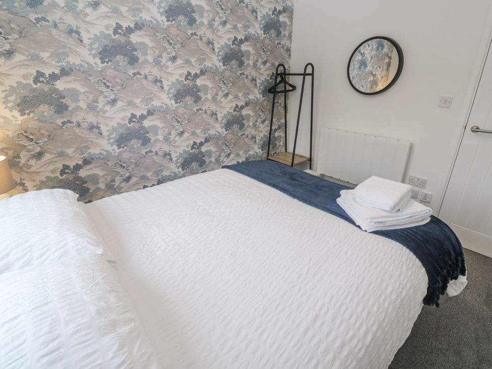 A bedroom with bed, towels, mirror and lamp at Chellowdene Cottage in Falmouth