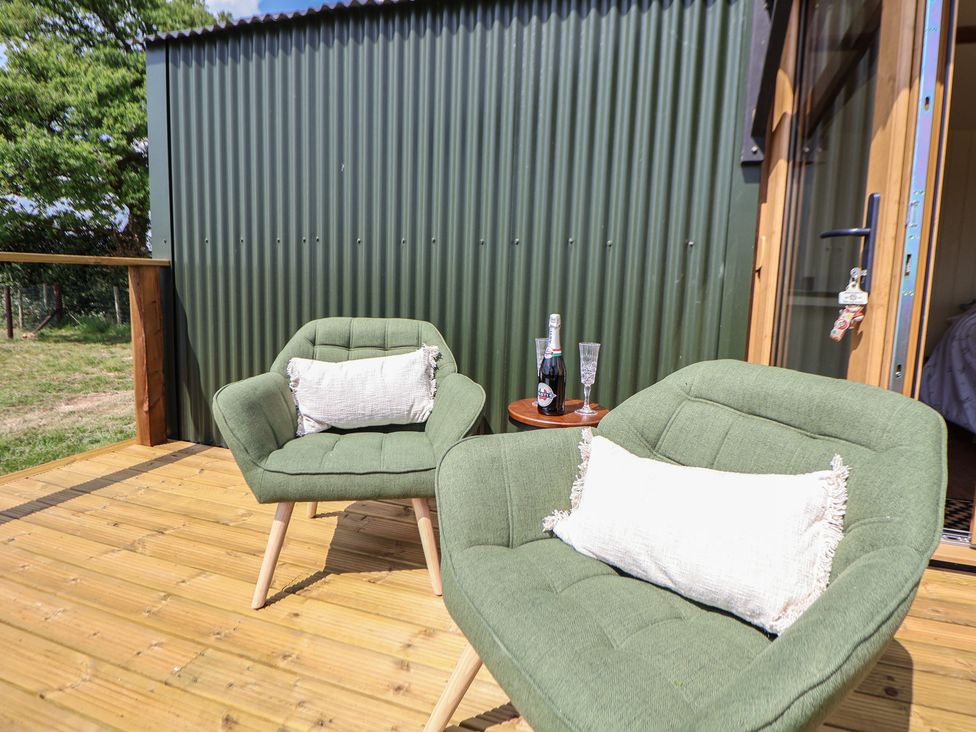 Two green cushioned chairs with white pillows on a wooden deck with a small table holding a bottle and two glasses at The Coop in Aston near Woore