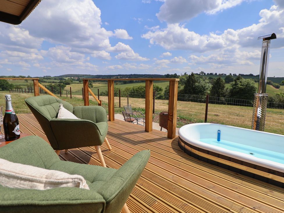 A wooden deck with two green armchairs a bottle a hot tub with water and a rural landscape at The Coop in Aston near Woore