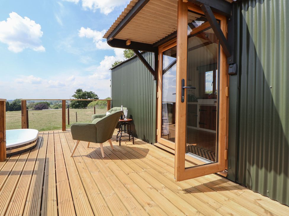A wooden deck with a green chair small table and glass door at The Coop in Aston near Woore