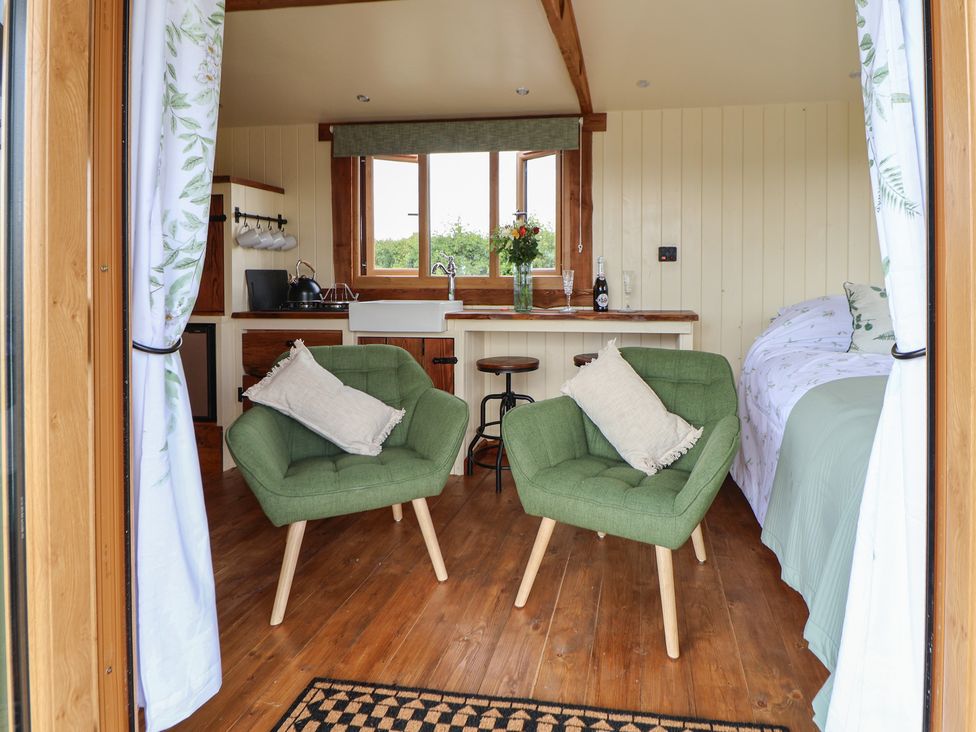 A small room with two green chairs, a bed, kitchen area with sink and stools at The Coop in Aston near Woore