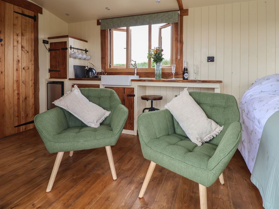 A room with two green armchairs with pillows a kitchen sink window and bed at The Coop in Aston near Woore