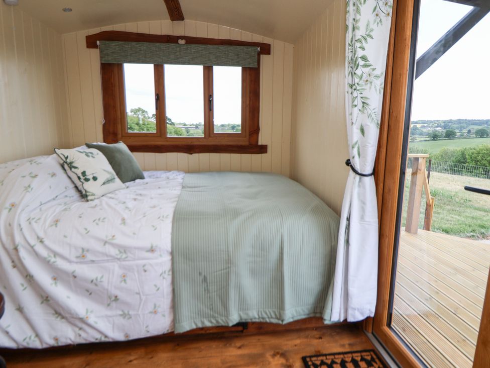 A bedroom with a bed covered in patterned bedding and pillows next to a window and a glass door leading to an outdoor deck at The Coop in Aston near Woore