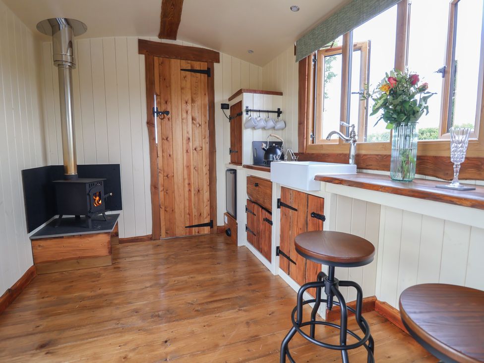 A kitchen with wooden floor and cabinets a small stove and a window with flowers at The Coop in Aston near Woore