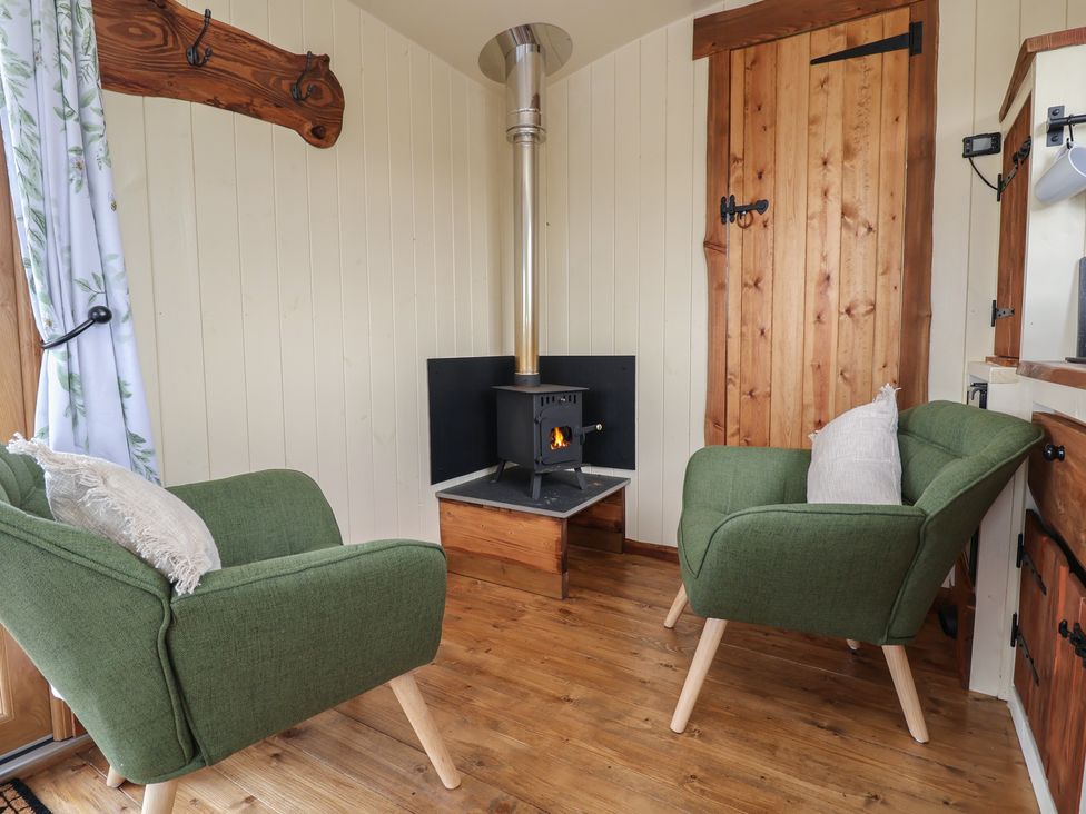 A small sitting area with two green armchairs a wood burning stove and a wooden door at The Coop Aston near Woore