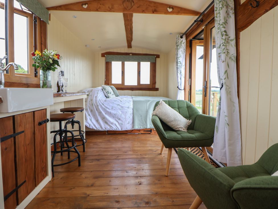 An interior view of a small room with a bed table stools green chairs and windows at The Coop in Aston near Woore