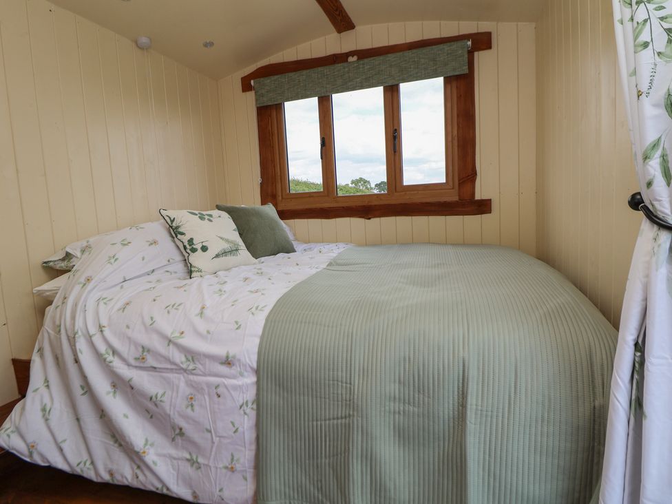 A bedroom with a bed covered in floral and green bedding next to a window at The Coop in Aston near Woore
