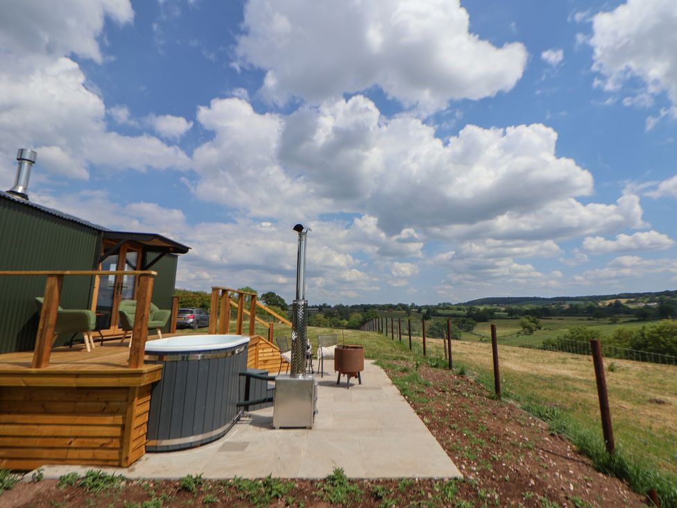 An outdoor area with a hot tub wooden deck chairs stove and fire pit overlooking fields at The Coop in Aston near Woore