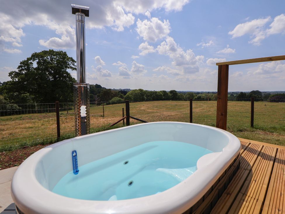 An outdoor hot tub on a wooden deck with a metal chimney and a field in the background at The Coop in Aston near Woore