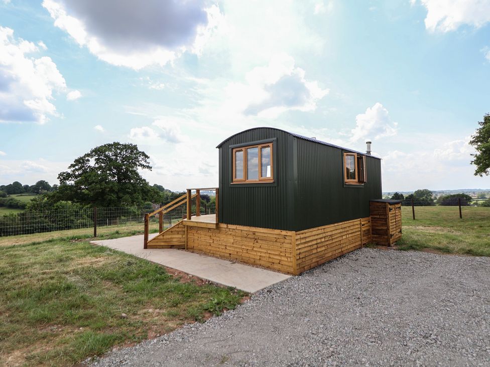 A small cabin on a wooden platform with gravel driveway and grassy field at The Coop in Aston near Woore