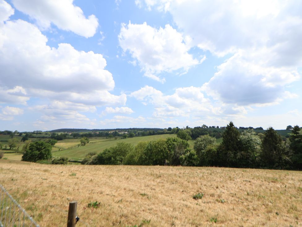 A rural field with dry grass and green trees under a partly cloudy sky in Aston near Woore