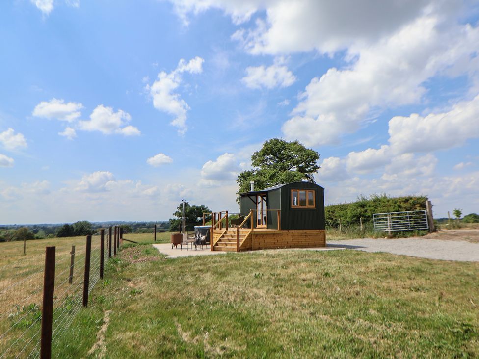 A small cabin on a wooden platform with a fenced grassy field under a blue sky at The Coop in Aston near Woore