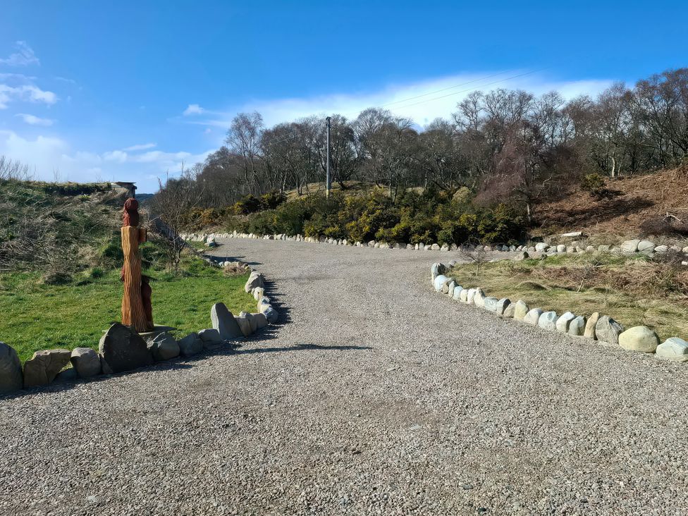 A gravel path bordered by stones and a wooden sculpture at Red Squirrel in Dornoch