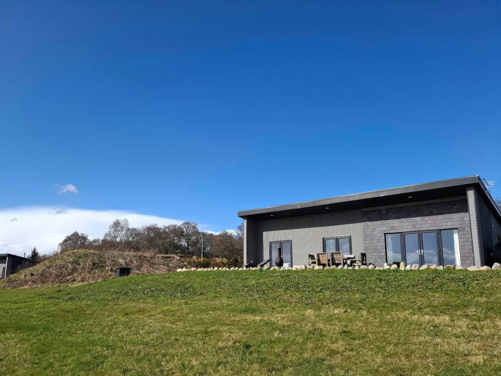 A house with a deck and furniture on the lawn at Red Squirrel in Dornoch