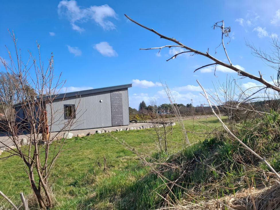A building with grass and trees surrounding it at Red Squirrel in Dornoch