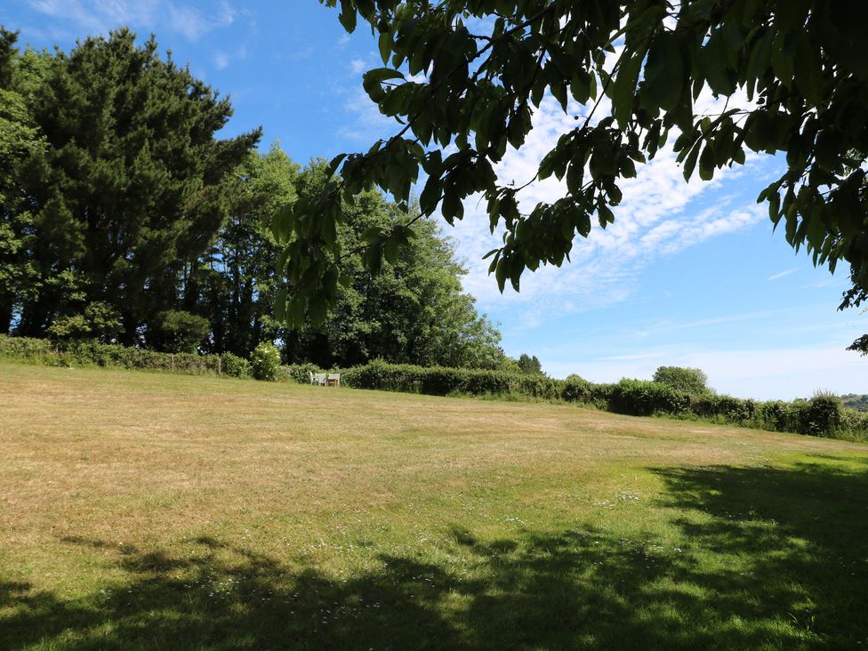 An outdoor area with grass, trees, and a bench at November Cottage in Dittisham