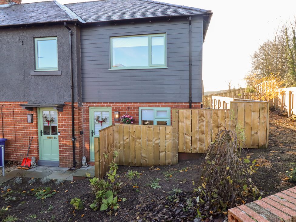 A house with green doors and windows next to a garden at Nene's Nest in Alnwick