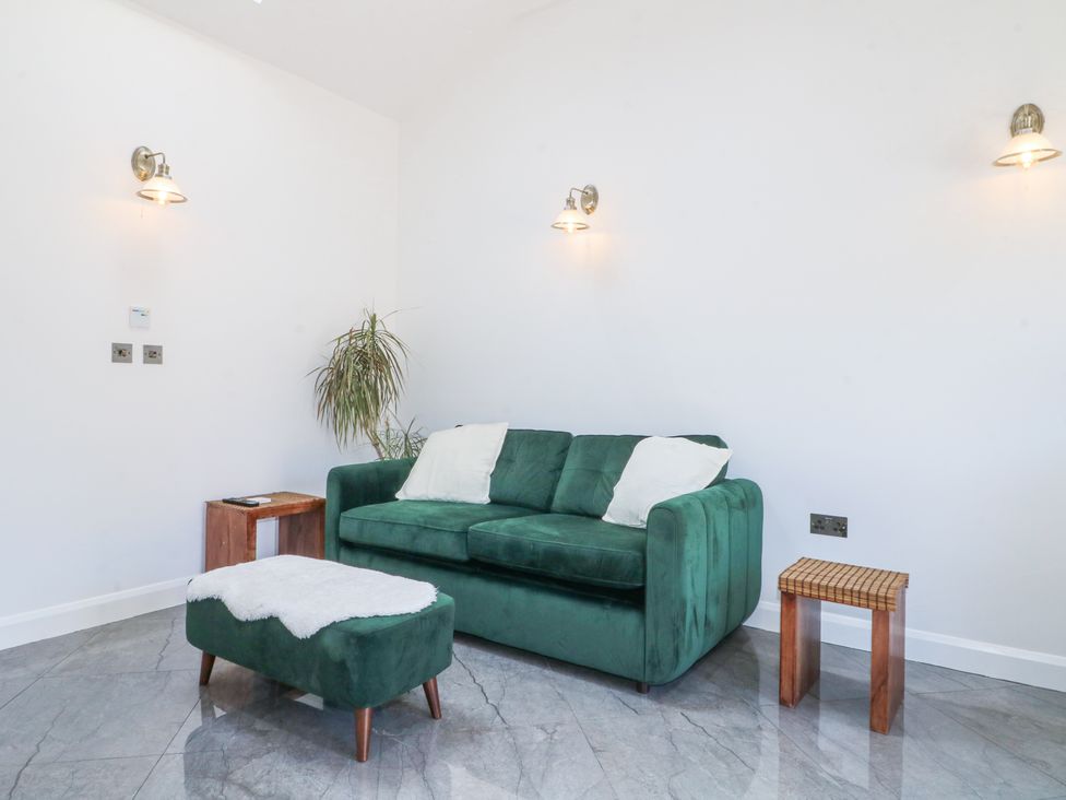 A green sofa with two white pillows a green footstool with a white cover two small wooden side tables and three wall-mounted lights in a living area at La Casa Lipa Nottingham