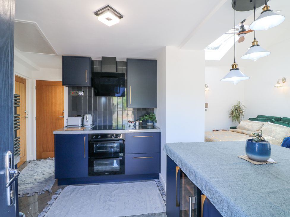 A kitchen with dark blue cabinets and a stove next to a dining table with a blue pot and a living area with a green sofa in La Casa Lipa Nottingham