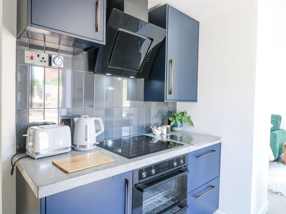 A kitchen countertop with a toaster kettle cutting board stovetop oven and blue cabinets at La Casa Lipa in Nottingham