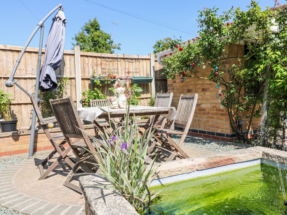An outdoor patio with wooden table and chairs a closed umbrella a small pond and plants at La Casa Lipa Nottingham