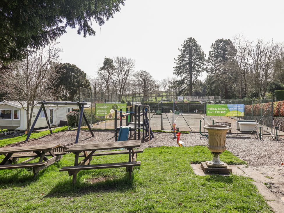 An outdoor play area with swings and picnic tables at Woodlands Retreat Llanfwrog near Ruthin