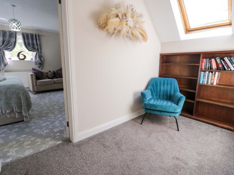 A reading nook with a blue chair and bookshelf at Woodlands Retreat in Llanfwrog near Ruthin