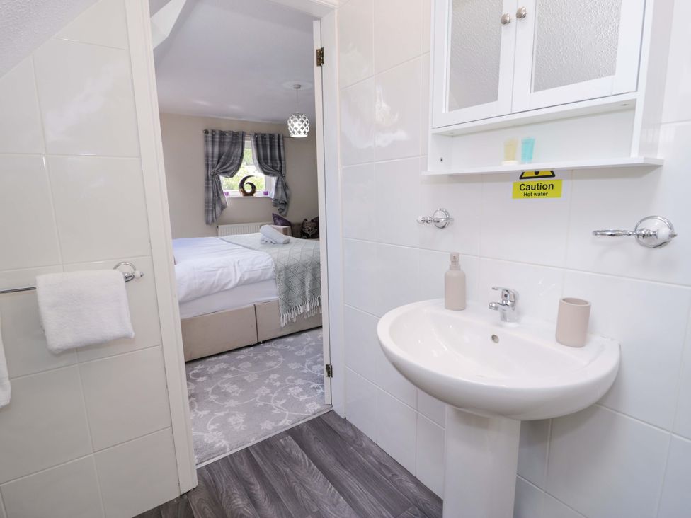 A bathroom with a wash basin and a bedroom door at Woodlands Retreat Llanfwrog near Ruthin