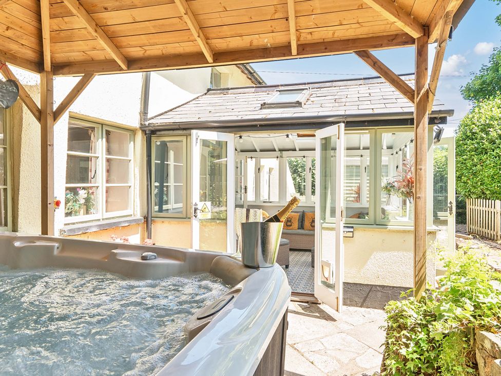 An outdoor area with a hot tub and glass doors leading to another room at 2 Pigsfoot Cottages Ash Thomas near Halberton, Devon