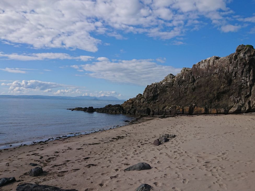 A beach with sand and rocks beside water at Learig Cottage Girvan