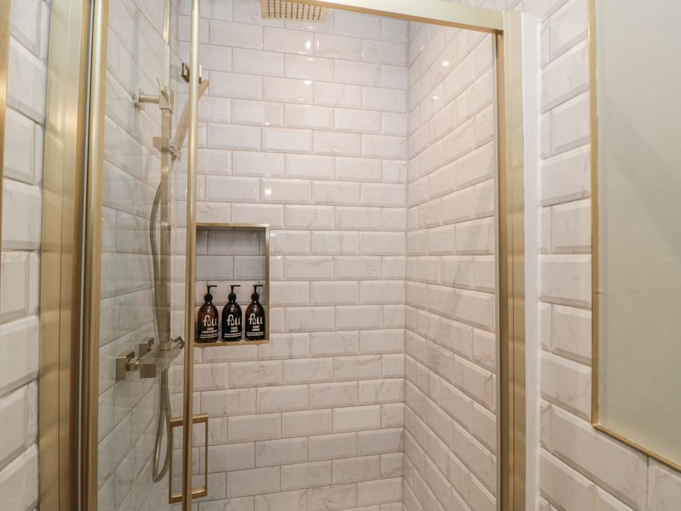 A shower with wall tiles and soap dispenser at Inglenook Cottage in Guisborough
