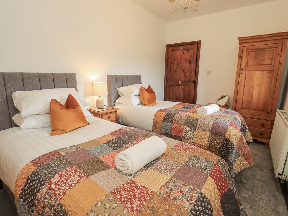 A bedroom with two beds and a wardrobe at Horse and Farrier Barn, Newton in Cartmel near Cartmel