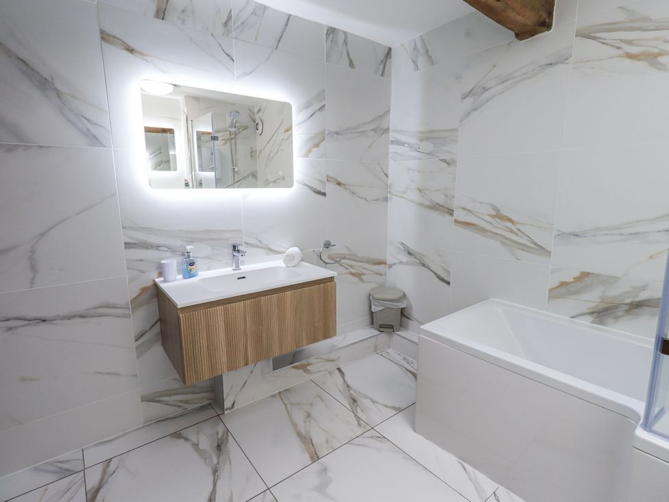A bathroom with a sink, bath tub, and a wall-mounted mirror at Horse and Farrier Barn in Newton in Cartmel near Cartmel