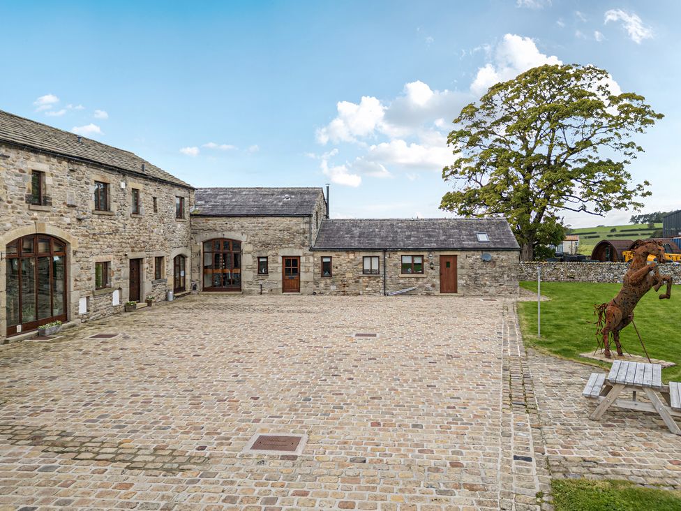 A stone building with a courtyard and sculpture at Orcaber Farmhouse in Austwick