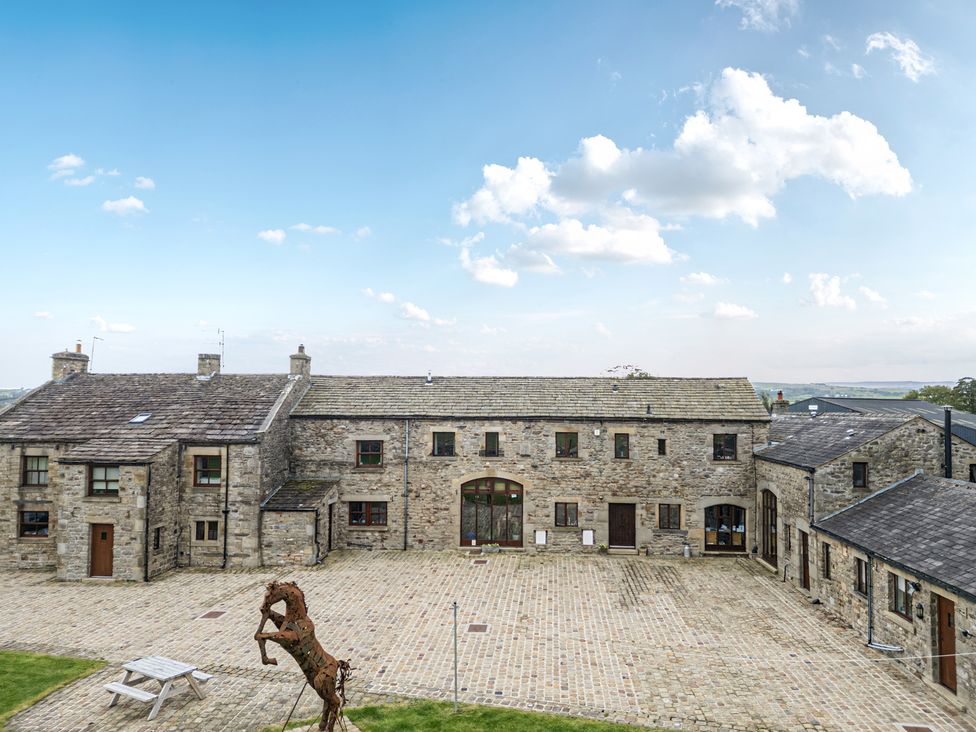 An outdoor view of stone buildings with a courtyard and a sculpture at Orcaber Farmhouse in Austwick