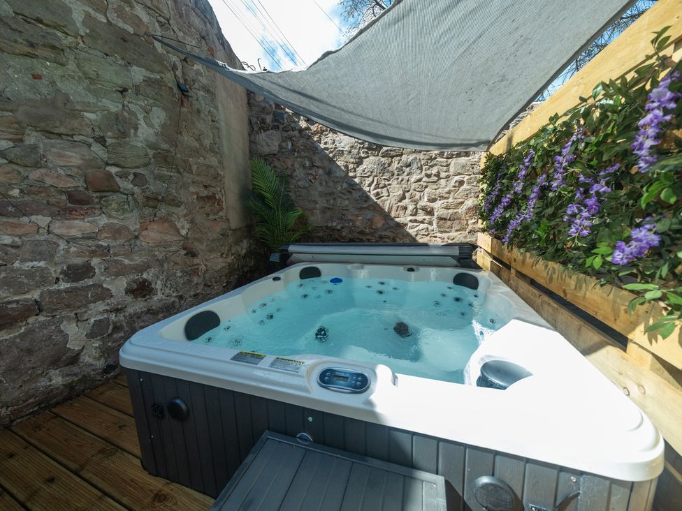 A hot tub surrounded by stone walls and plants at Wonderland in Tweedmouth, Berwick-Upon-Tweed