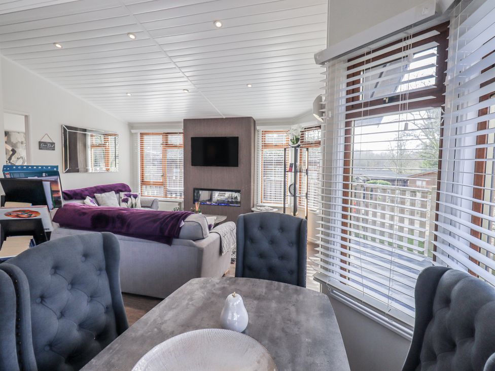 A living room with a television and dining table at JacMar Lodge, 14 Applethwaite, Limefitt Park near Windermere