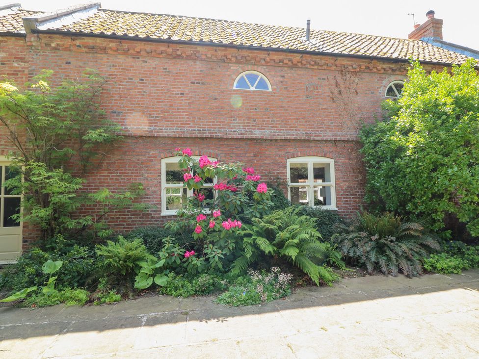 An outdoor view of a brick wall with windows and flower bushes at The Old Barn in Caenby near Market Rasen