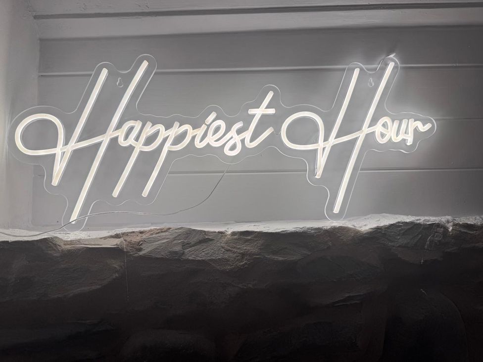 A neon sign that says Happiest Hour at The Studio Cottage near Denbigh