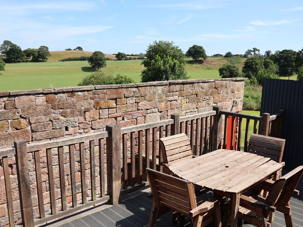 An outdoor area with a wooden table and chairs overlooking a field at 1 Fountain Cottages in Peckforton, Tarporley