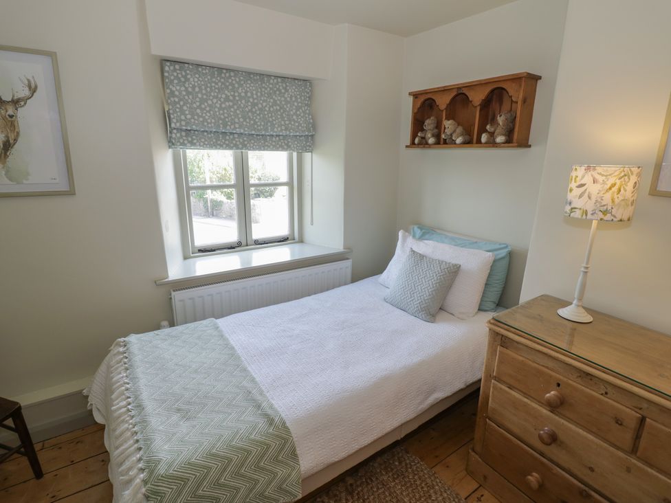 A bedroom with a bed, dresser, lamp, and window at Robins Nest in Bourton-On-The-Water