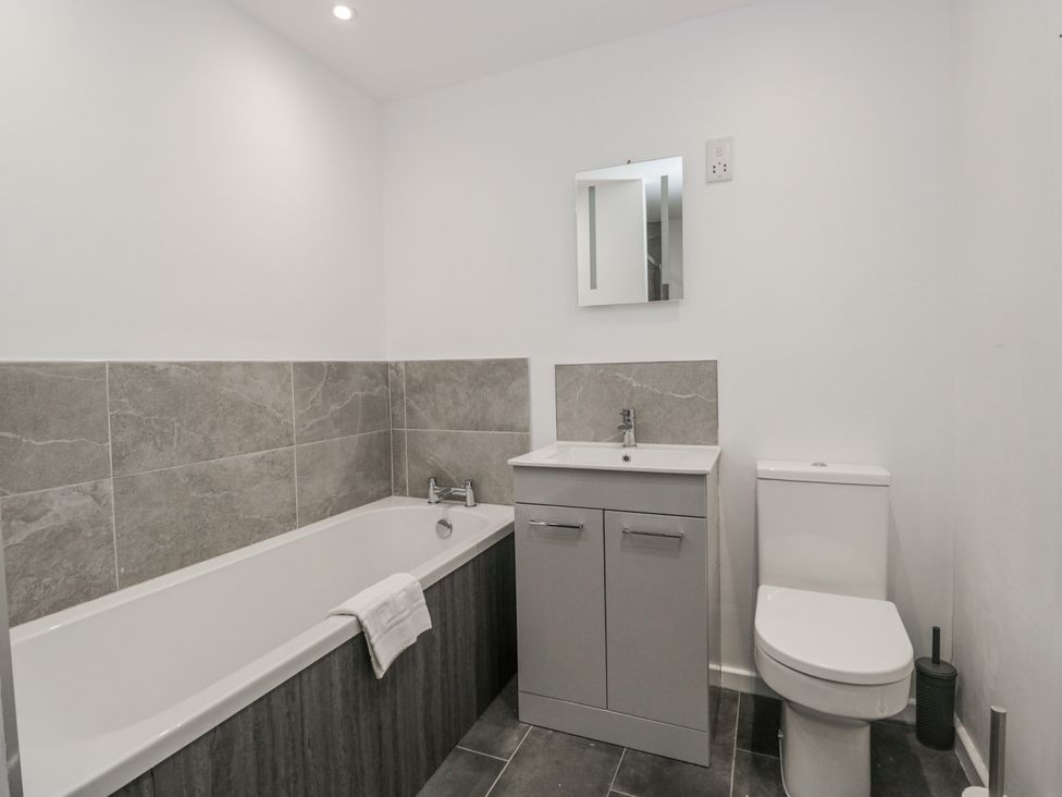 A bathroom with a bathtub, toilet, sink and mirror at Clarence House in Dalton-In-Furness
