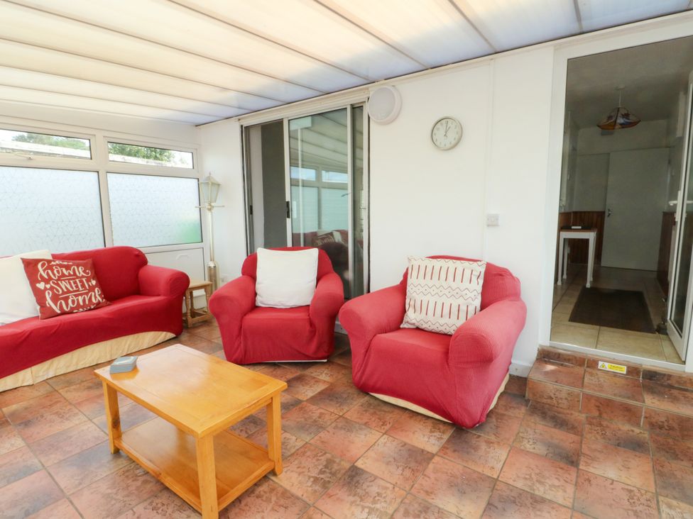 A conservatory with red sofas and a coffee table at Pen Bonc in Llanddaniel Near Gaerwen