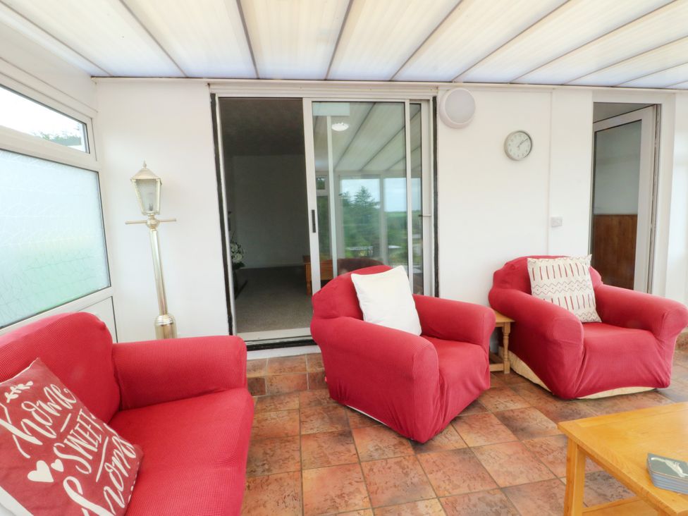 A conservatory with red armchairs and a wooden table at Pen Bonc Llanddaniel Near Gaerwen