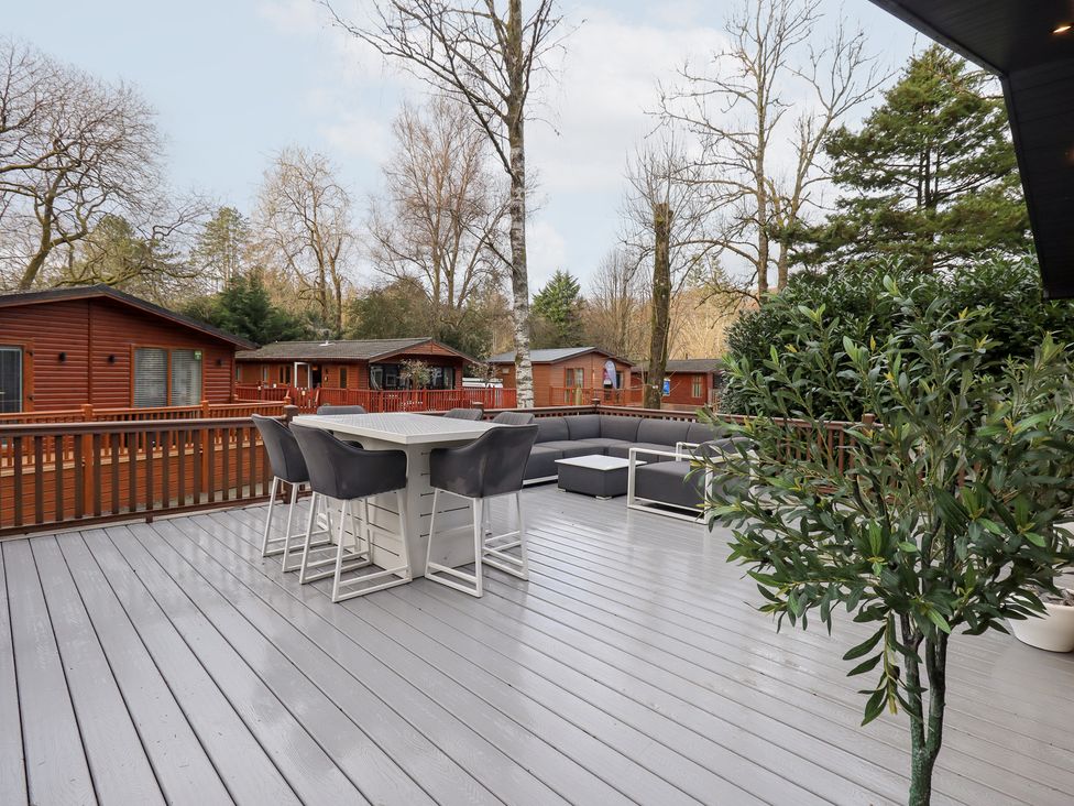 An outdoor deck with furniture and trees at Unique Luxury Lodge, 1 Langdale, White Cross Bay near Windermere