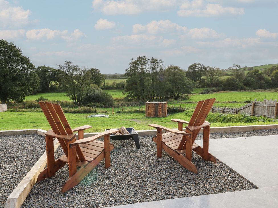A seating area with chairs and a fire pit overlooking a field at Ty Crwn in Lampeter