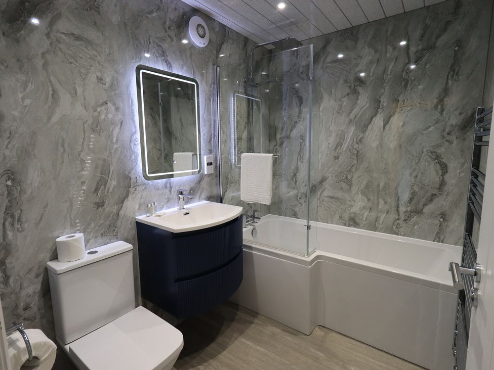 A bathroom with a bathtub, toilet, sink, and mirror at Whitbarrow 24 in Penruddock
