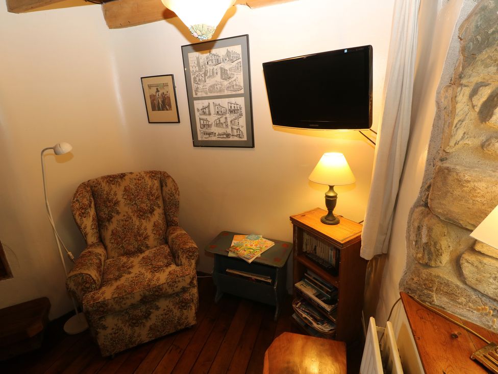 A snug with an armchair, TV, lamp, and bookshelf at Penfeidr Newydd in Carningli Common, Newport, Pembrokeshire