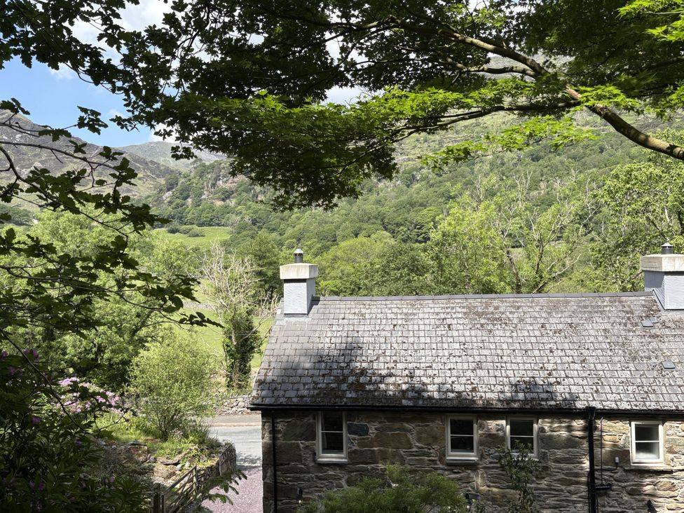 A house with a stone roof and trees in the foreground at Glyn Awel, Nant Gwynant near Beddgelert