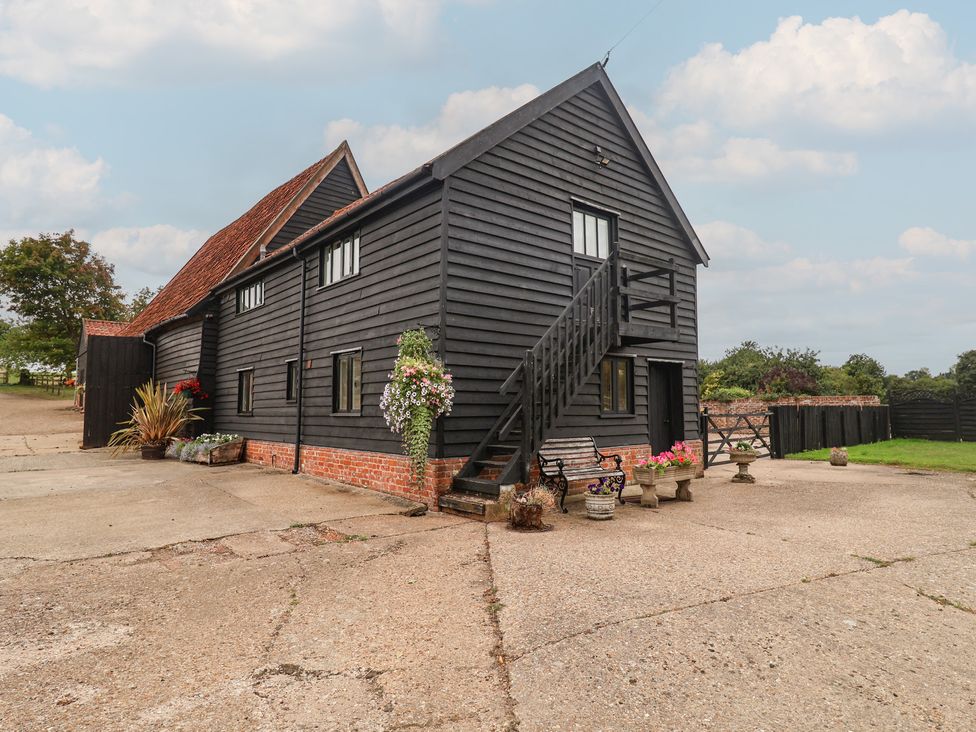 An outdoor view of a black barn with steps and flower pots at The Cow Shed in Chediston near Halesworth